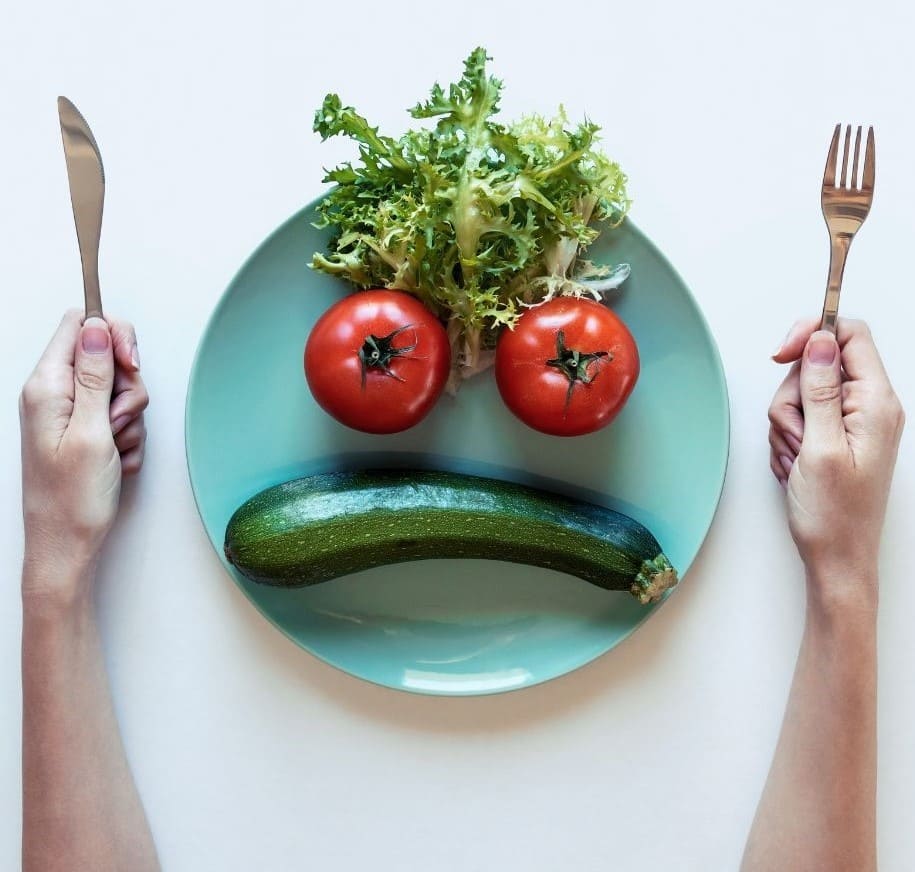 Assiette avec légumes tomates courgette et salade qui forme un visage mécontent Diététicienne Perte de poids Micronutrition