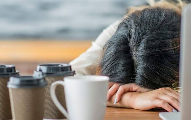 Tête d'une fille couchée sur son bureau car elle est fatiguée avec plusieurs tasses de café devant elle